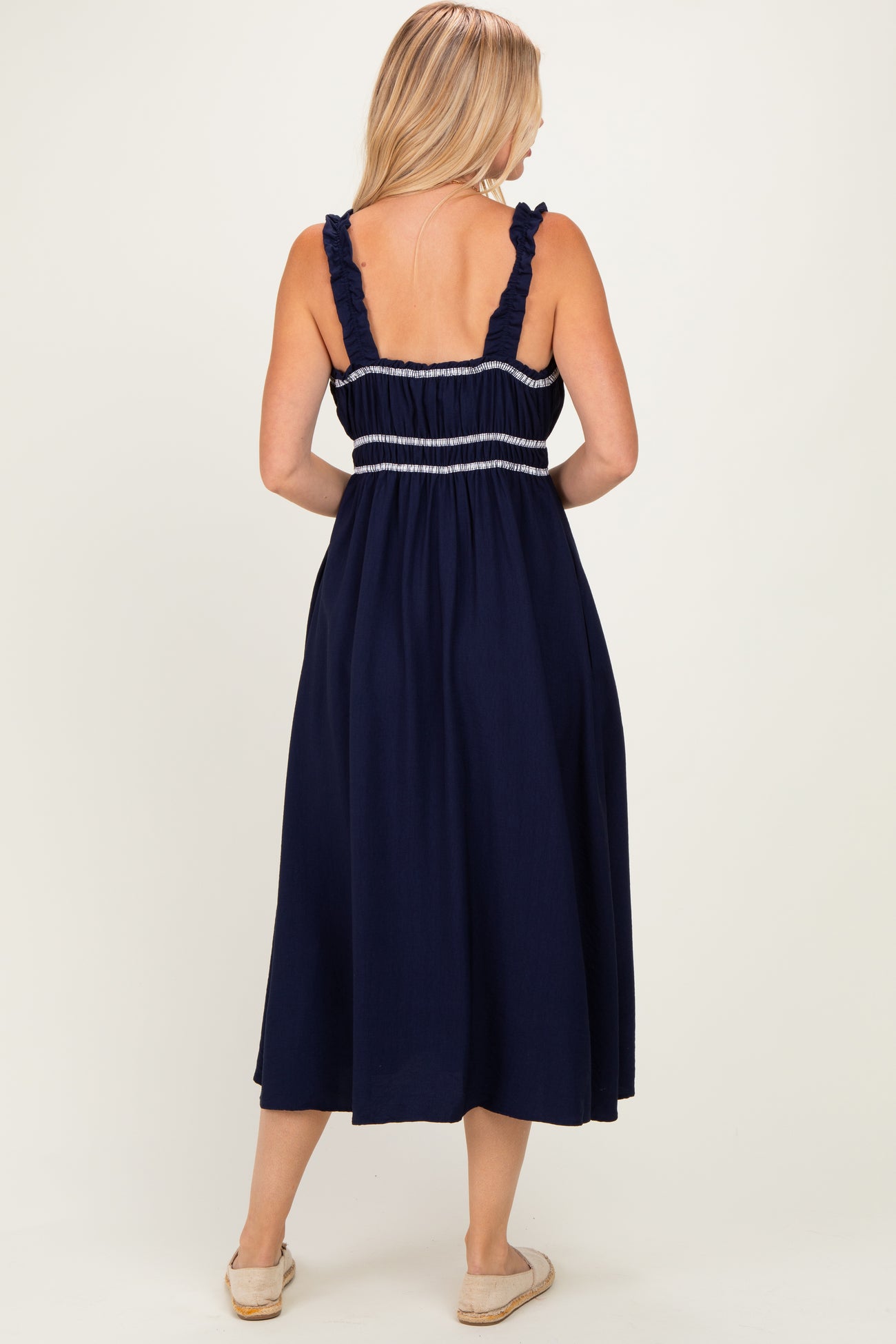 woman wearing a navy blue maxi dress with ruffled straps and smocked bodice, seen from the back
