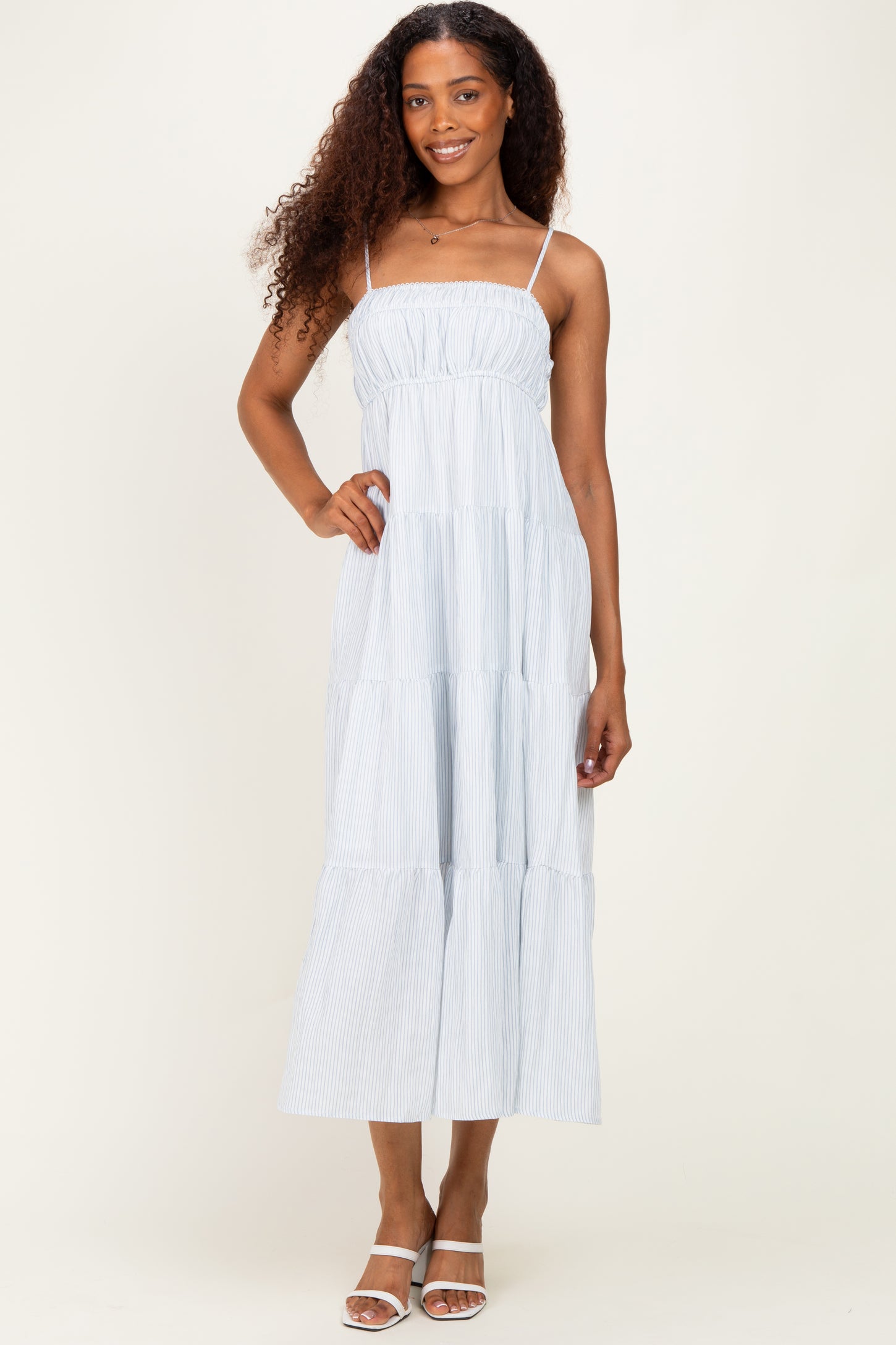 woman wearing a light blue striped maxi dress with spaghetti straps and a tiered ruffle design