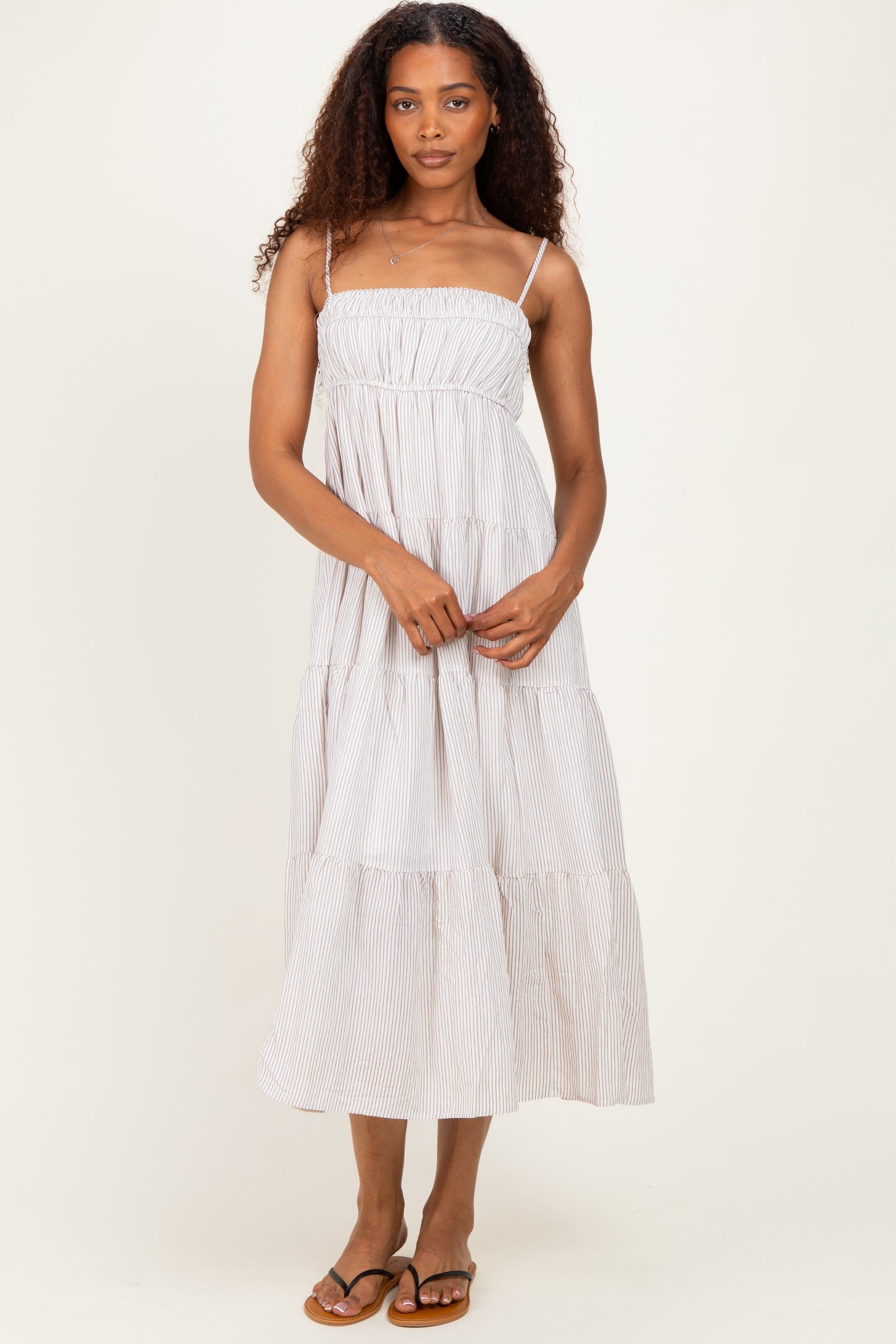 woman wearing a striped maxi dress with spaghetti straps and tiered ruffles, standing with hands in front