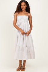 woman wearing a striped maxi dress with spaghetti straps and tiered ruffles, standing with hands in front
