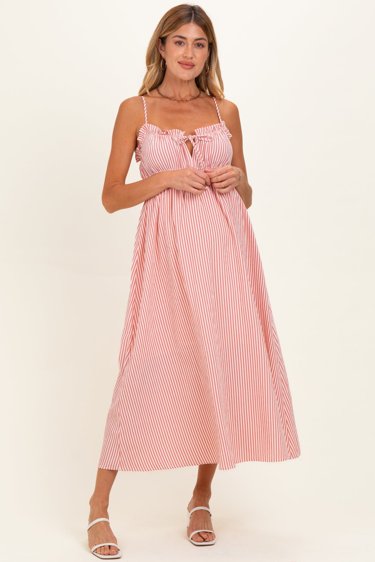 woman wearing a pink and white striped maternity dress with adjustable straps and a tie detail at the bust