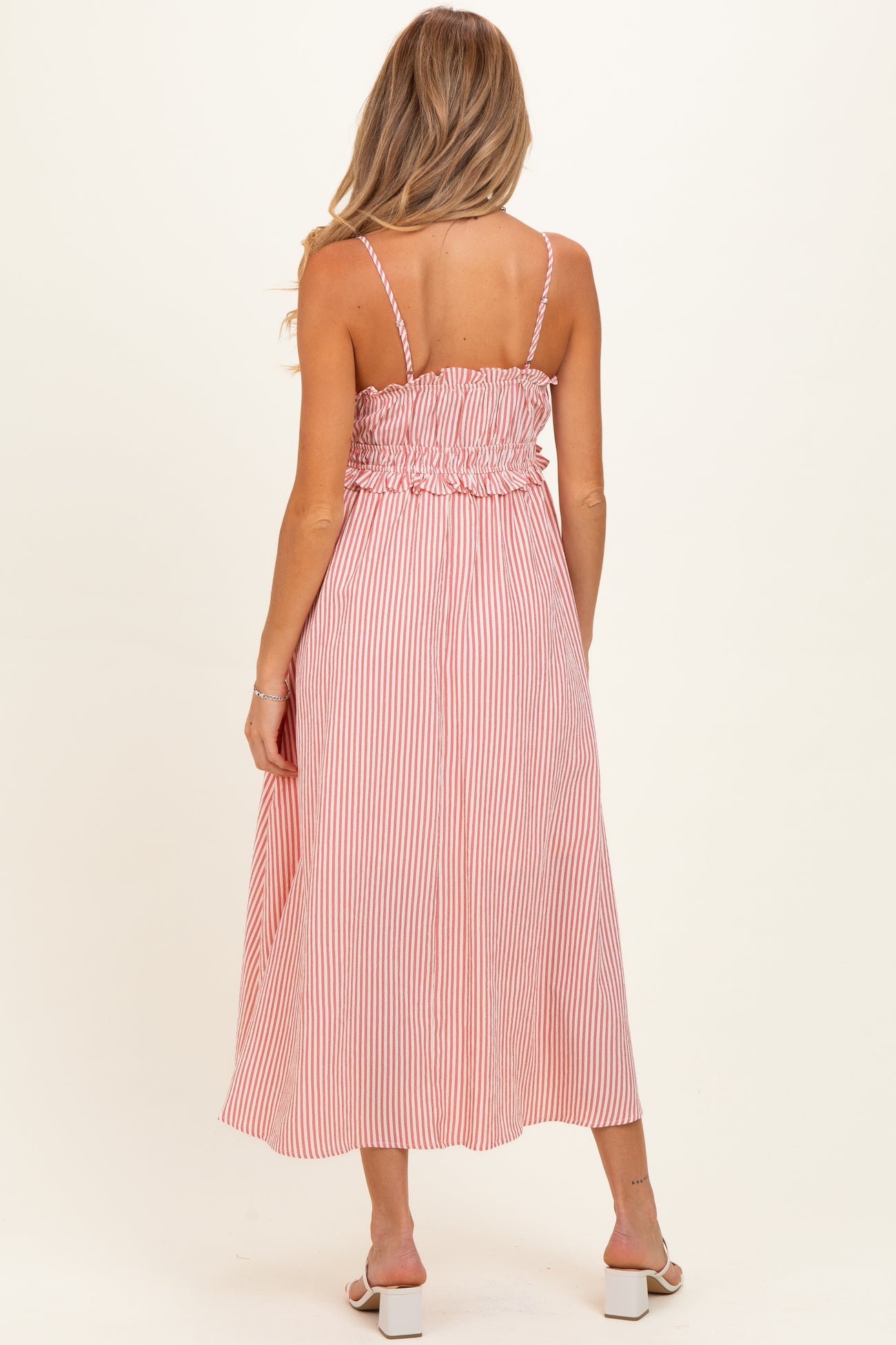 woman wearing a pink and white striped maternity maxi dress with a smocked back and adjustable straps, showing her baby bump