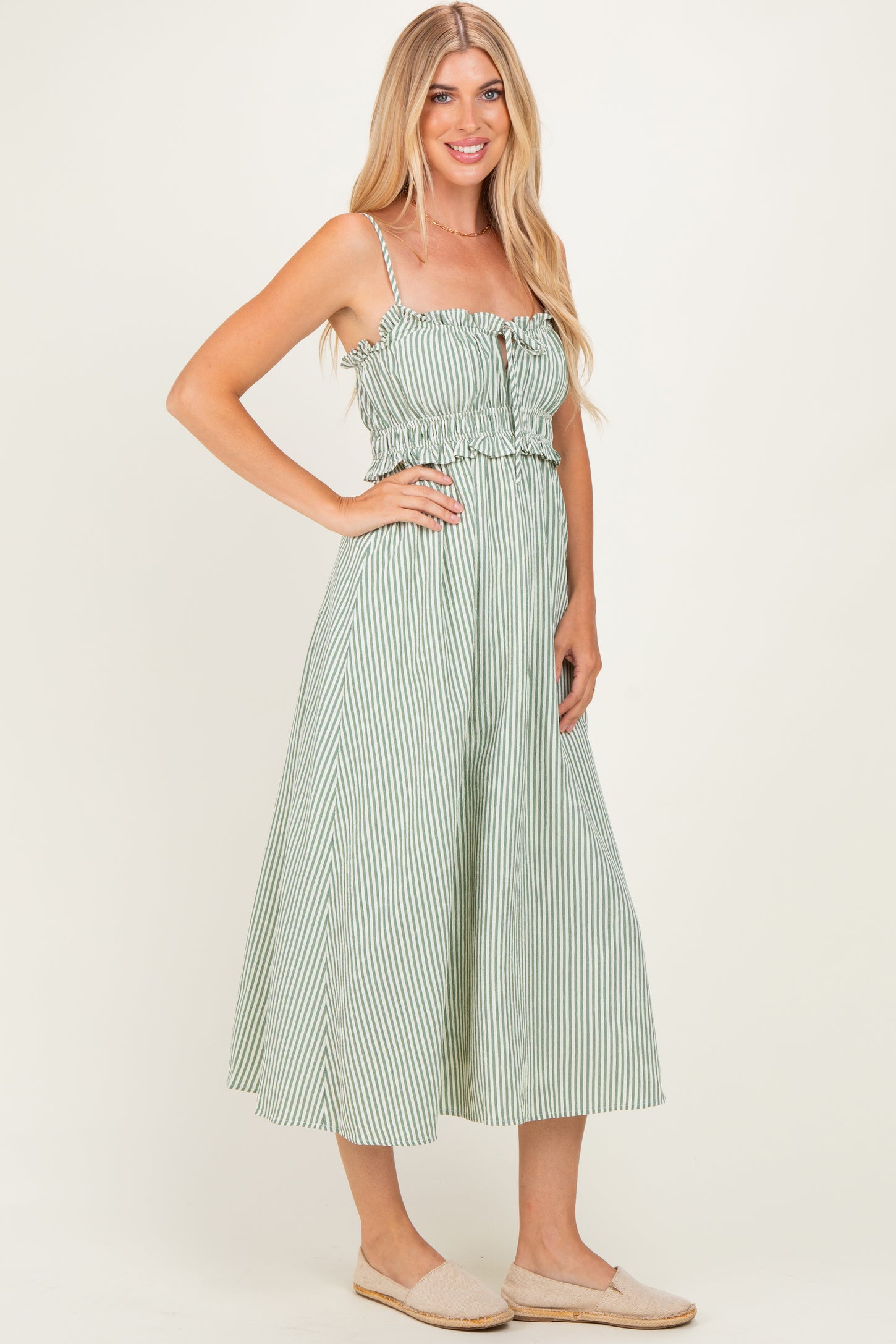 woman wearing a green and white striped midi dress with spaghetti straps and a ruffled bodice, standing in a relaxed pose