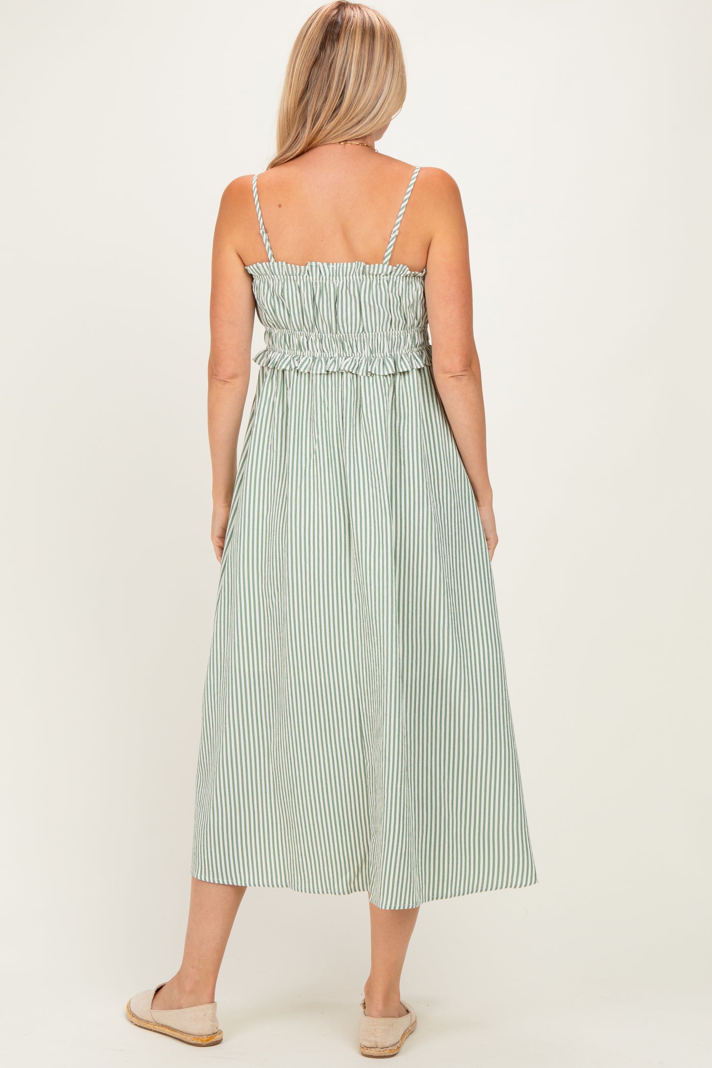 woman wearing a green and white striped maxi dress with smocked bodice and ruffle detail, standing with back to the camera