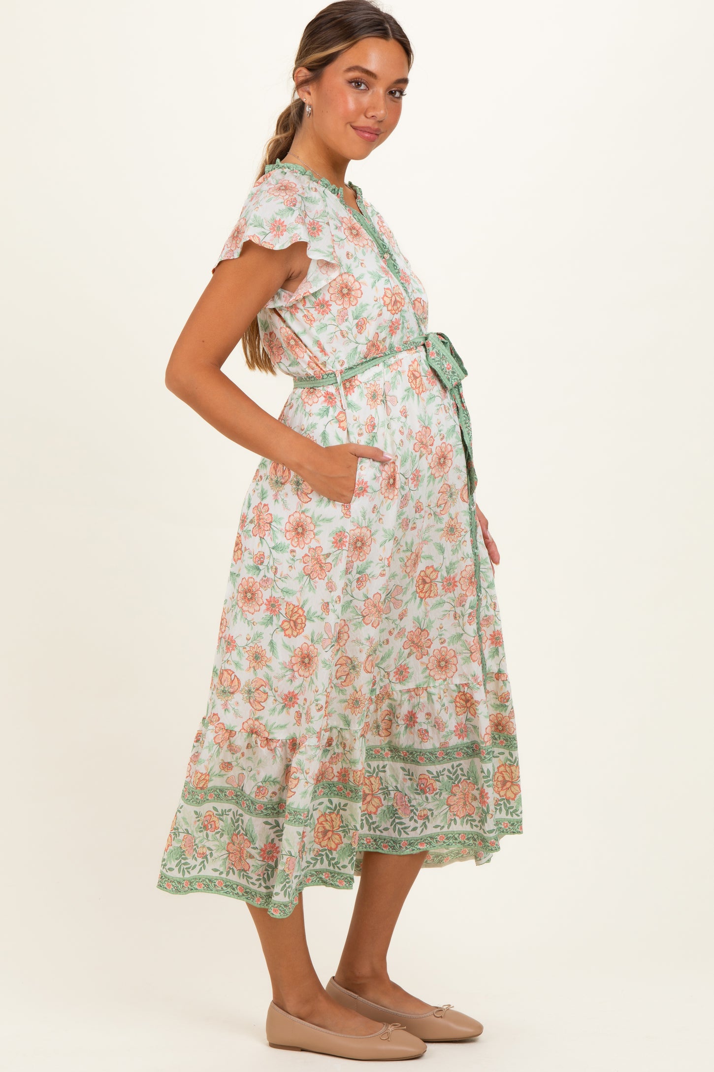 woman wearing a floral maternity wrap dress with short sleeves and a tie belt, featuring pockets and a flowing skirt
