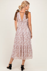 woman wearing a floral midi dress with v-back and bow tie straps in light pink and brown colors
