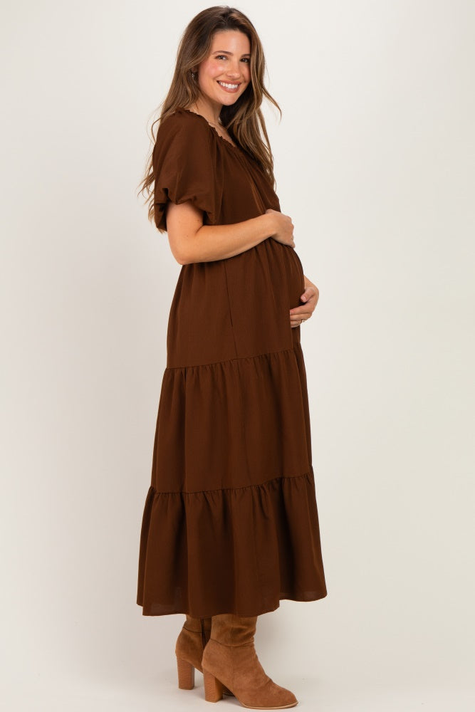 woman wearing a brown tiered maternity dress and cradling her baby bump