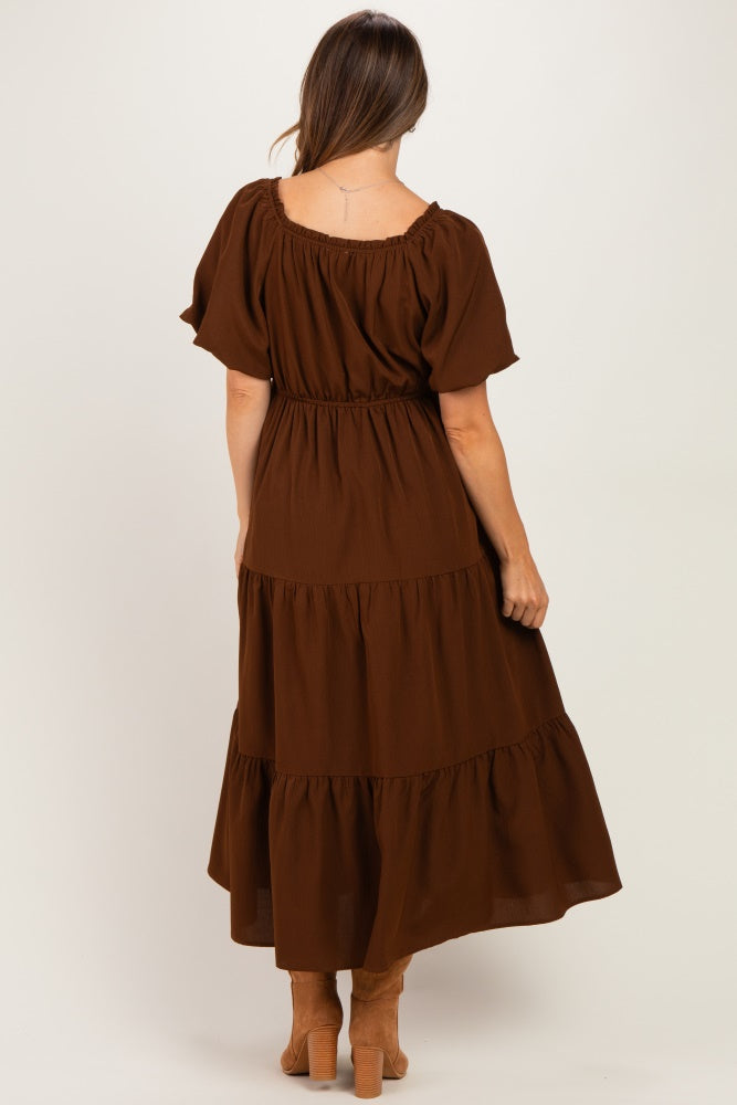 woman wearing a brown tiered maxi maternity dress with short sleeves and a fitted waist, showing a baby bump