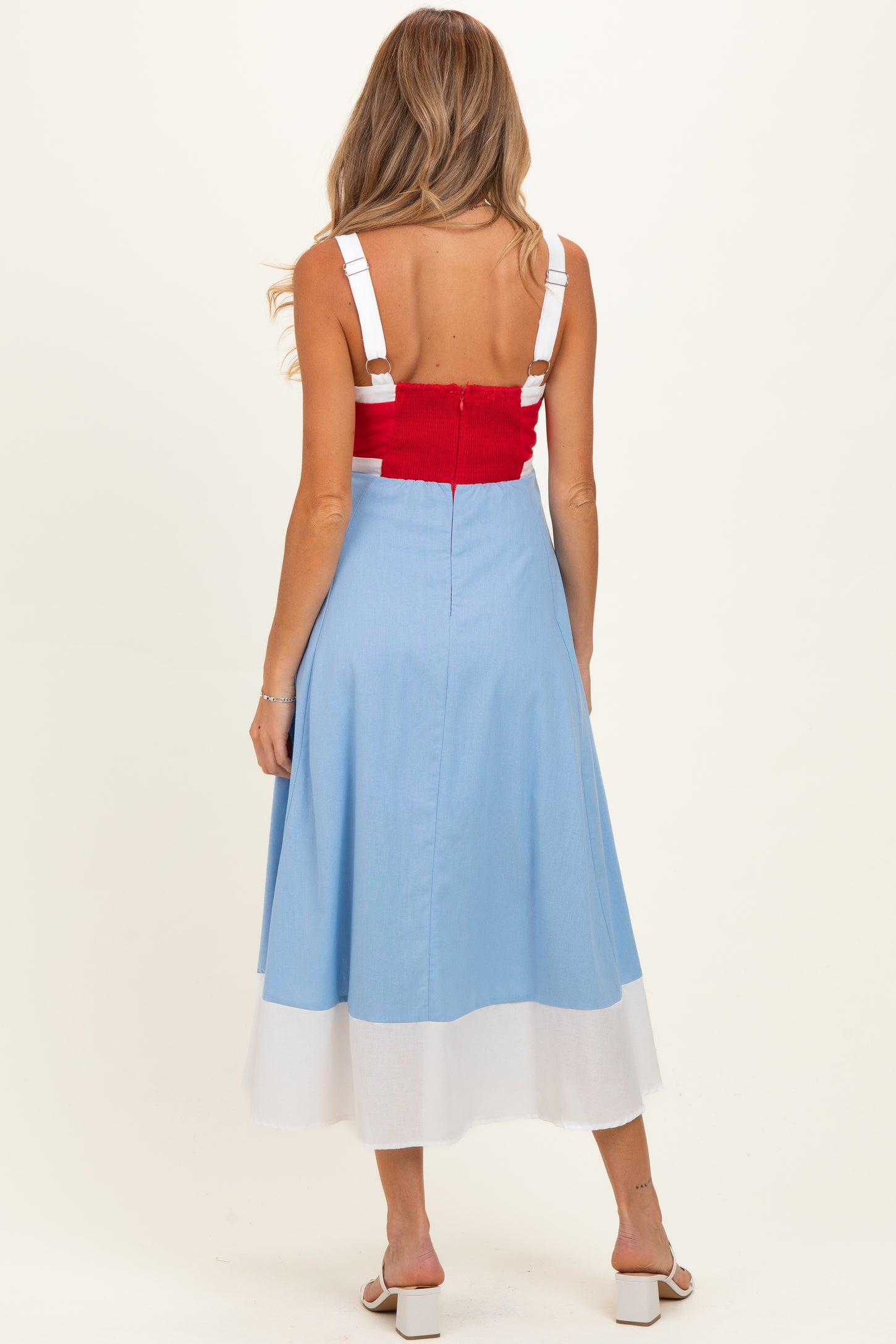 woman wearing a red cropped top and a blue and white color-blocked midi skirt, showcasing her baby bump from behind