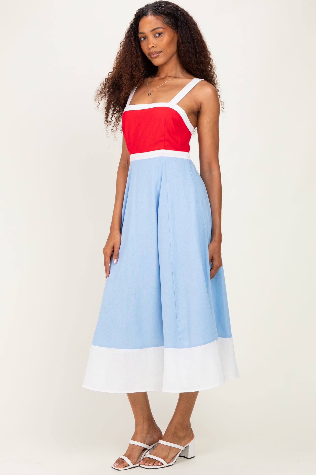 woman wearing a spaghetti strap color block midi dress with red, blue, and white sections and white sandals
