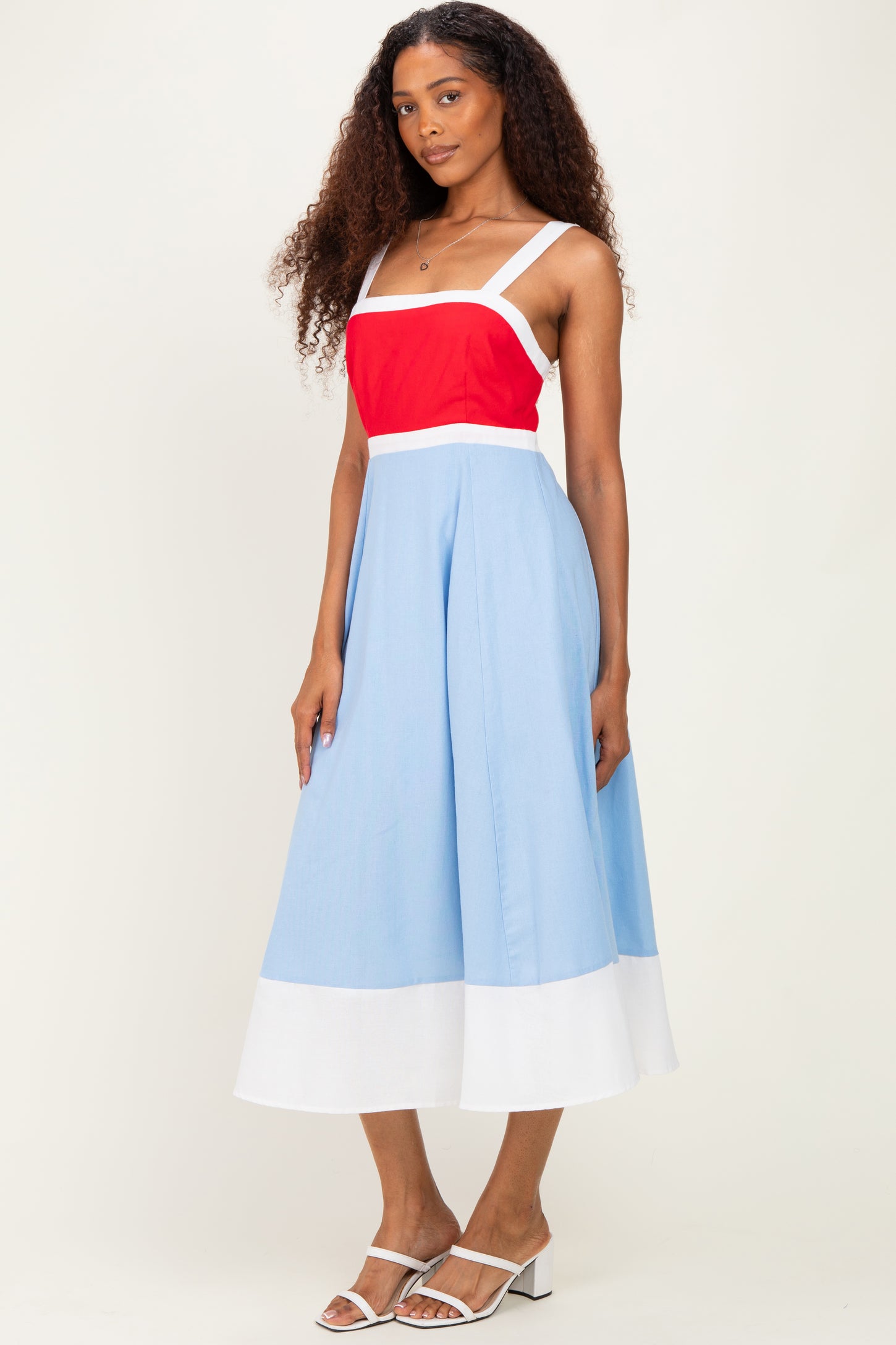 woman wearing a spaghetti strap color block midi dress with red, blue, and white sections and white sandals