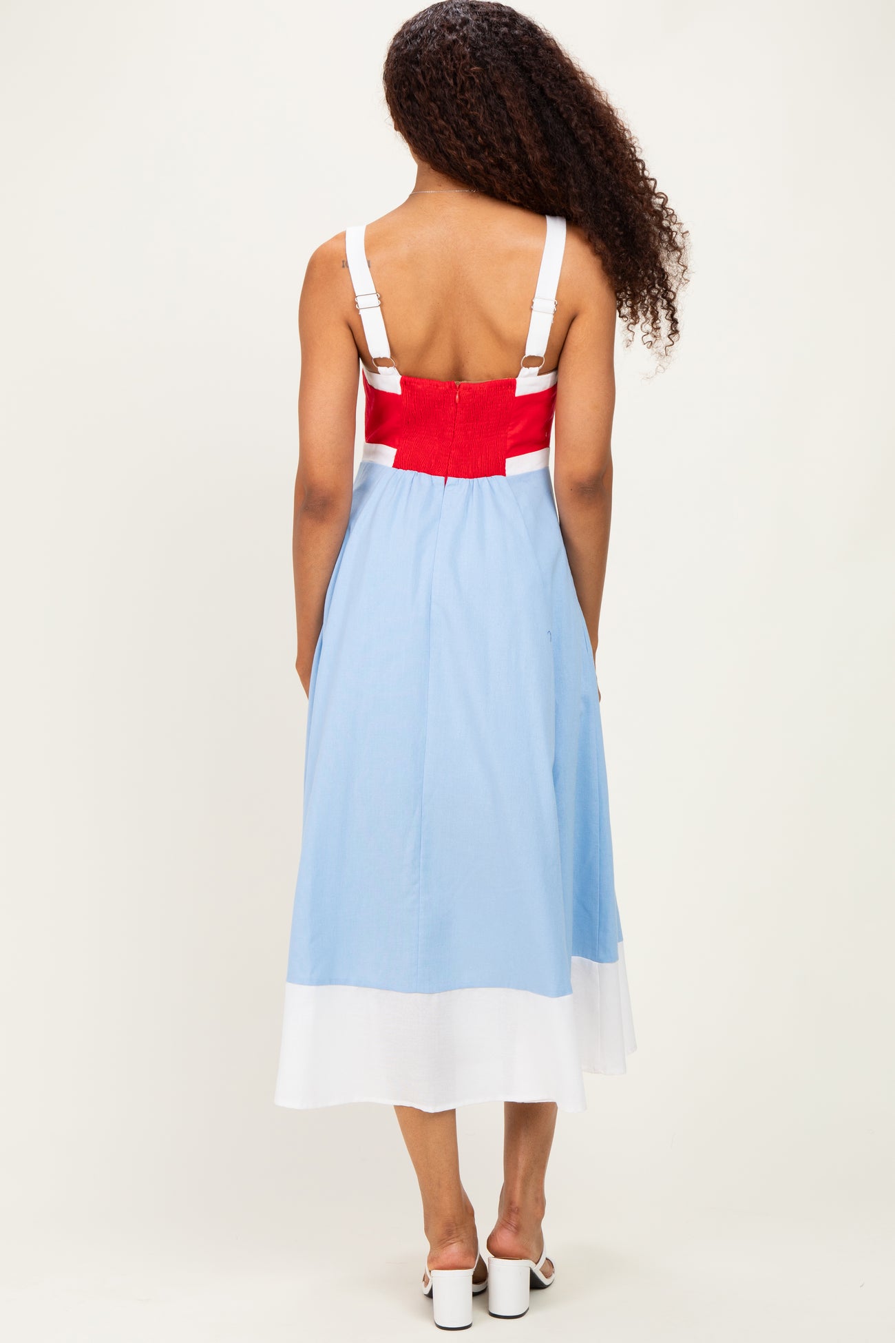 woman wearing a light blue sleeveless midi dress with a red and white color block detail on the back