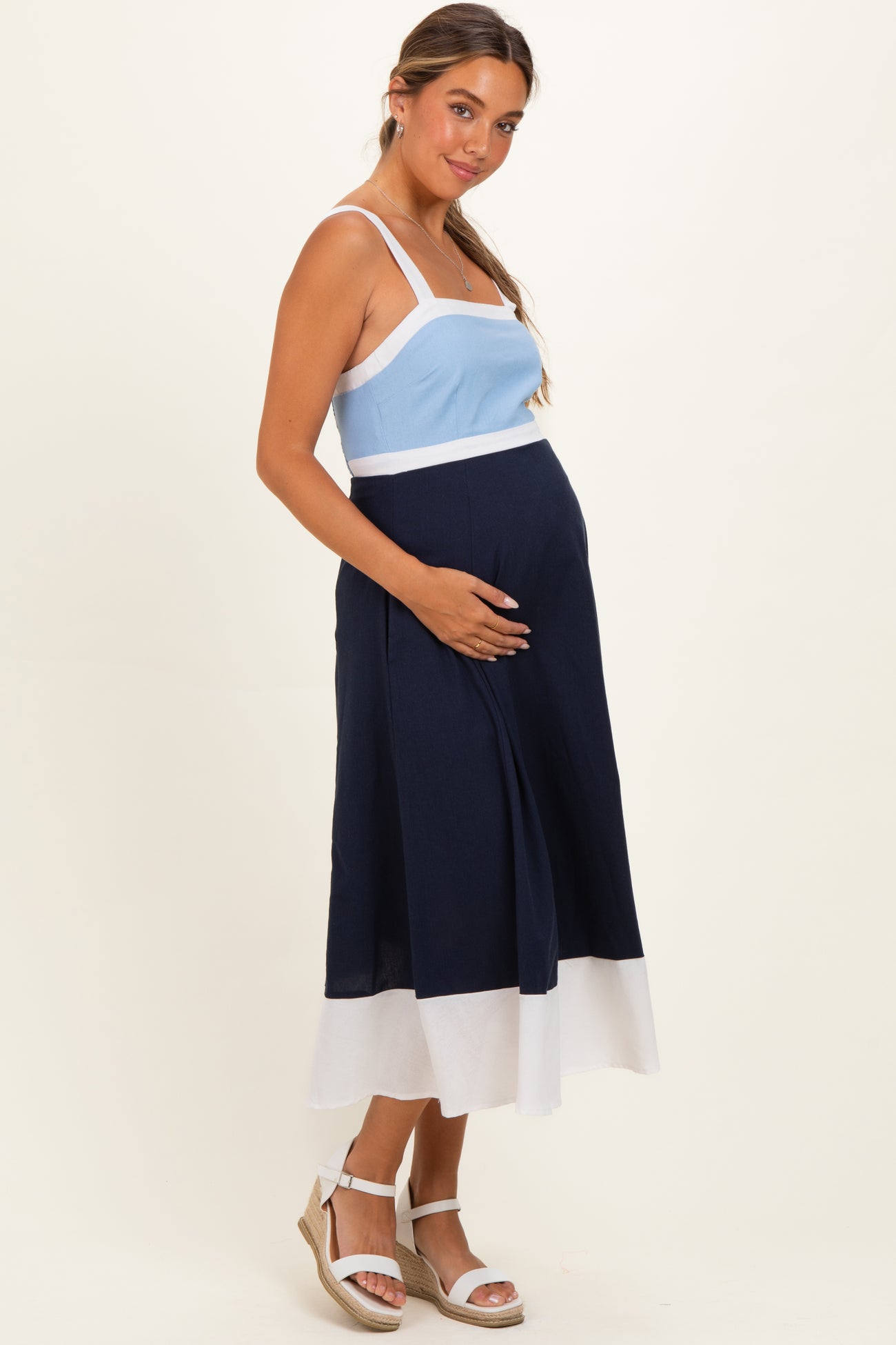woman wearing a light blue and navy maternity dress, holding her baby bump with a smile