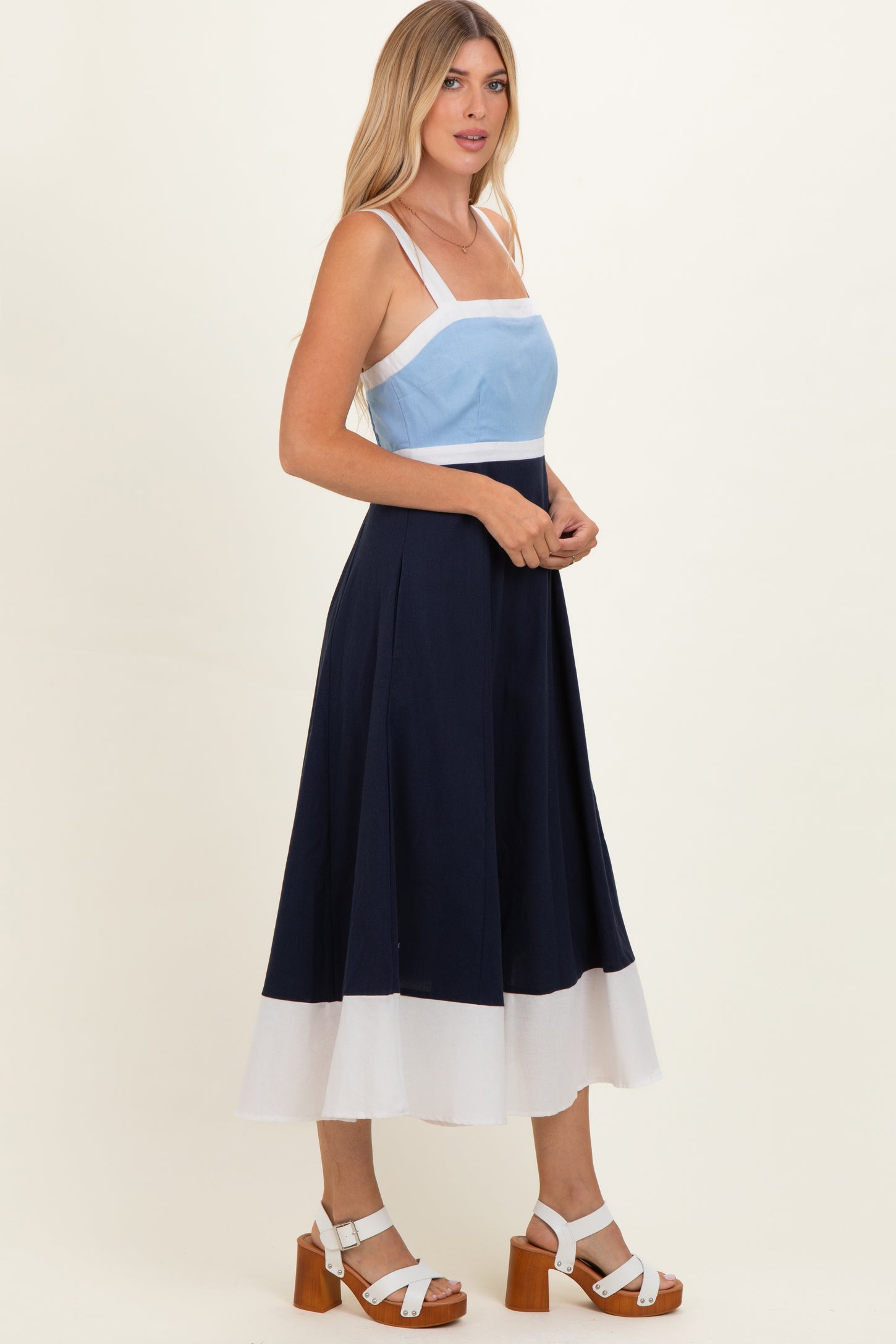 woman wearing a color-blocked midi dress with a light blue bodice and navy skirt, styled with white accents and platform sandals