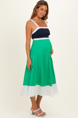 woman wearing a navy and white maternity top with a green and white midi skirt, holding her baby bump