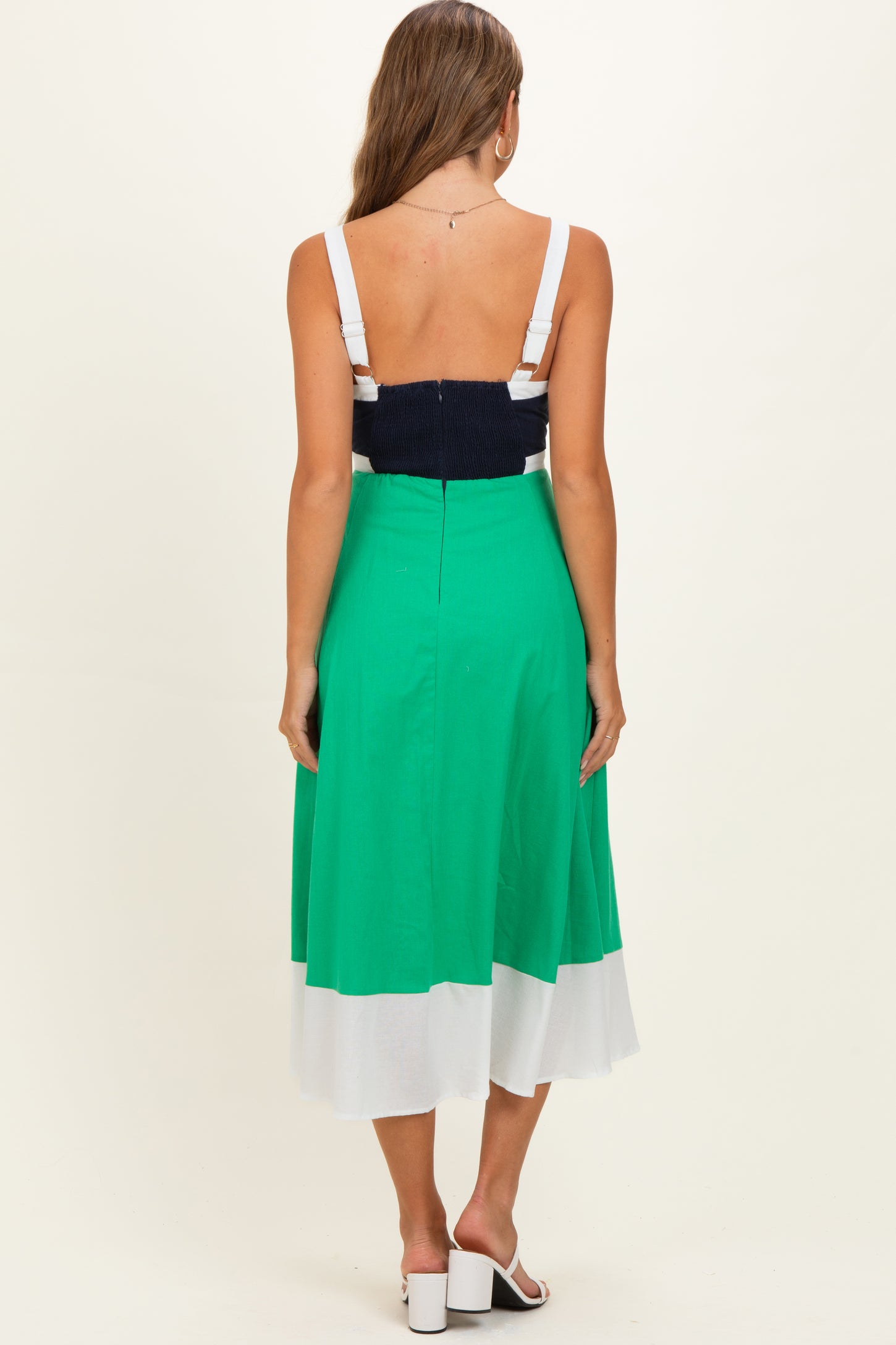 woman wearing a color-blocked green and white maternity dress with a navy blue bodice, showing her back