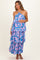 woman wearing a pink and blue floral print maternity dress with tiered layers and a halter neckline, holding her baby bump