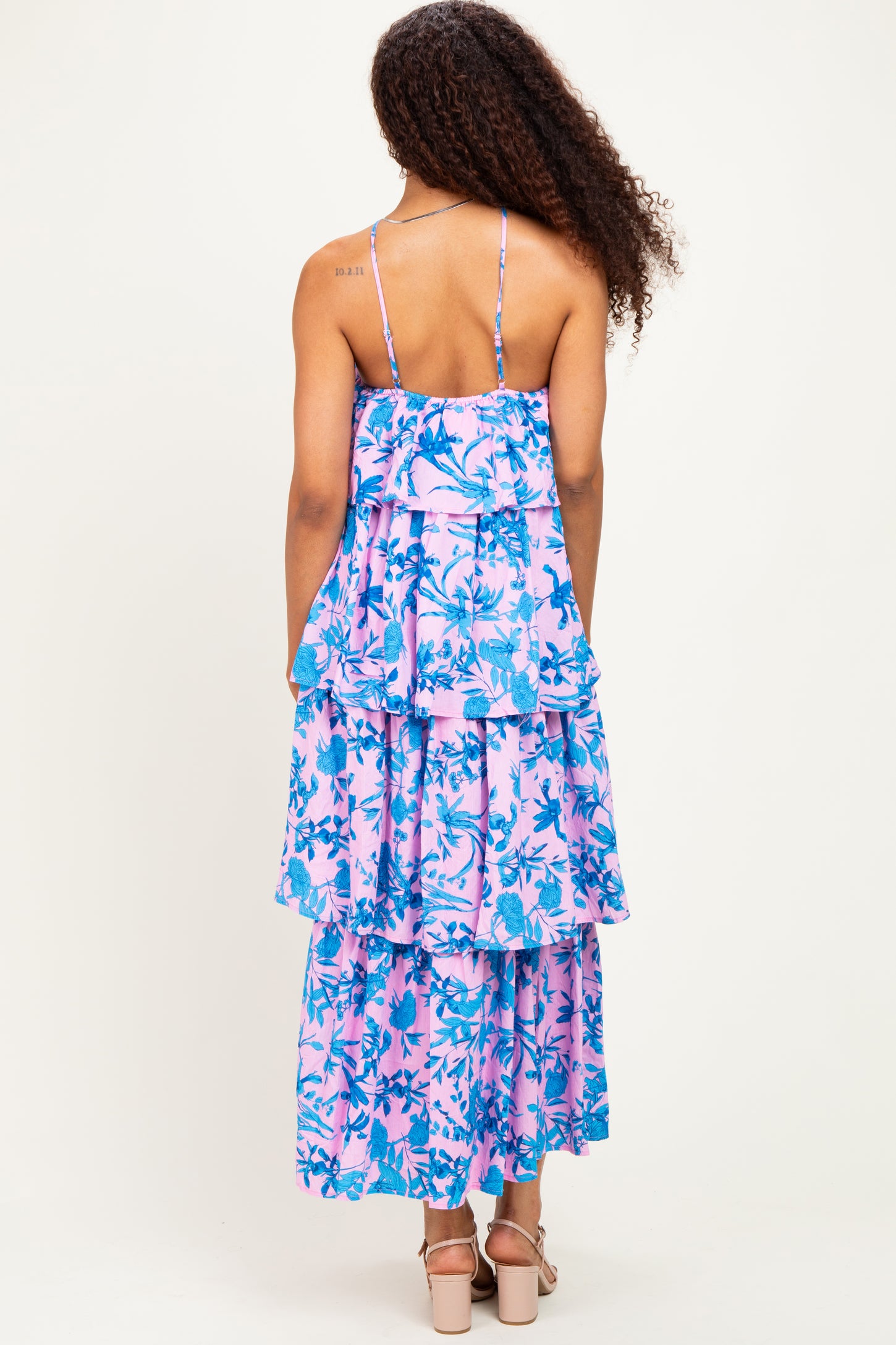 woman wearing a back view of a pink and blue tiered maxi dress with spaghetti straps and floral pattern