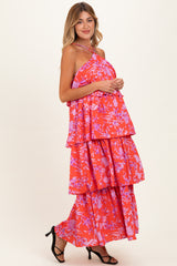 woman wearing a bright red floral maternity maxi dress with tiered layers and sandals, holding her baby bump