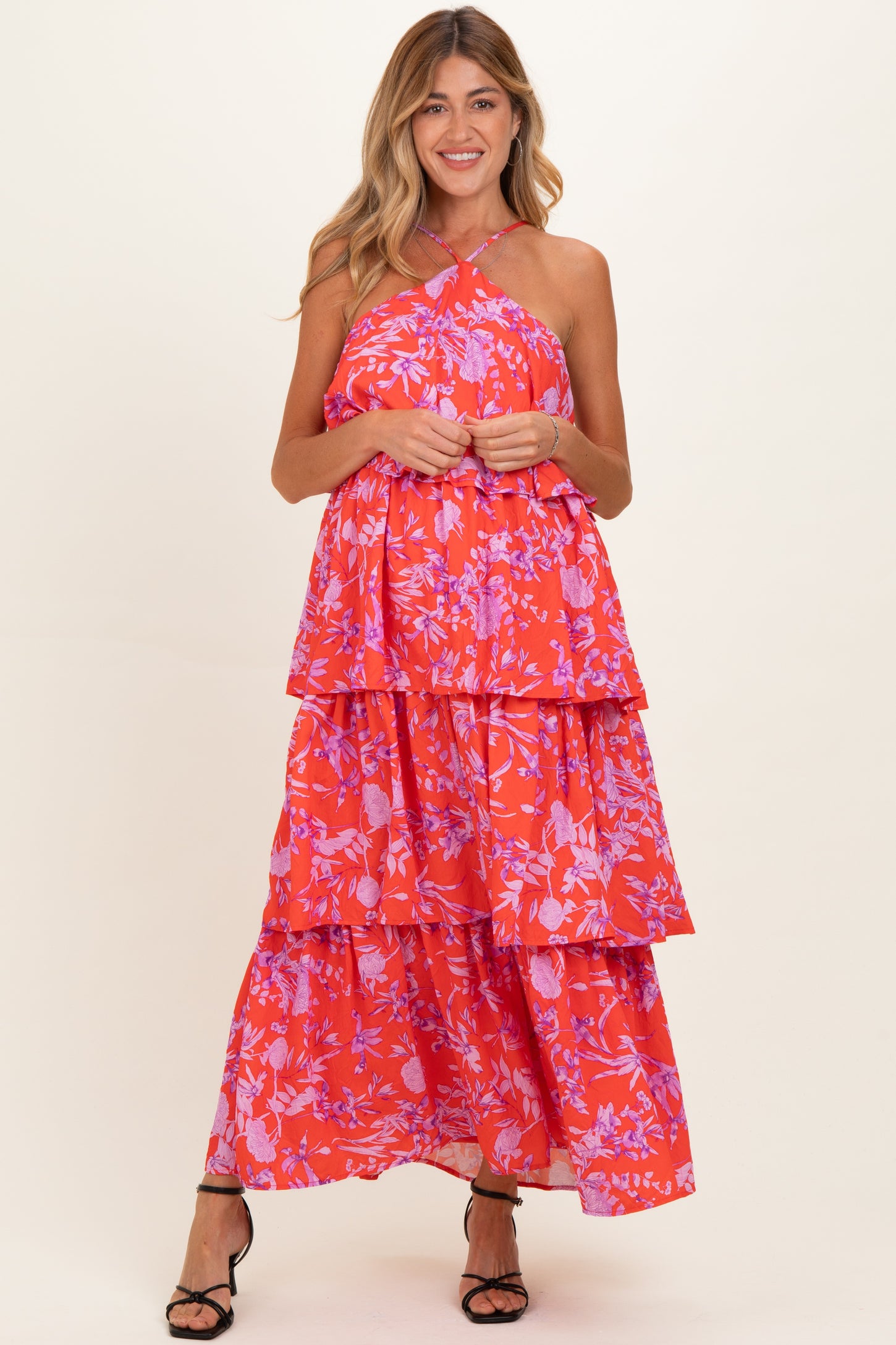 woman wearing a strapless red floral maxi maternity dress with layered tiers and smiling at the camera