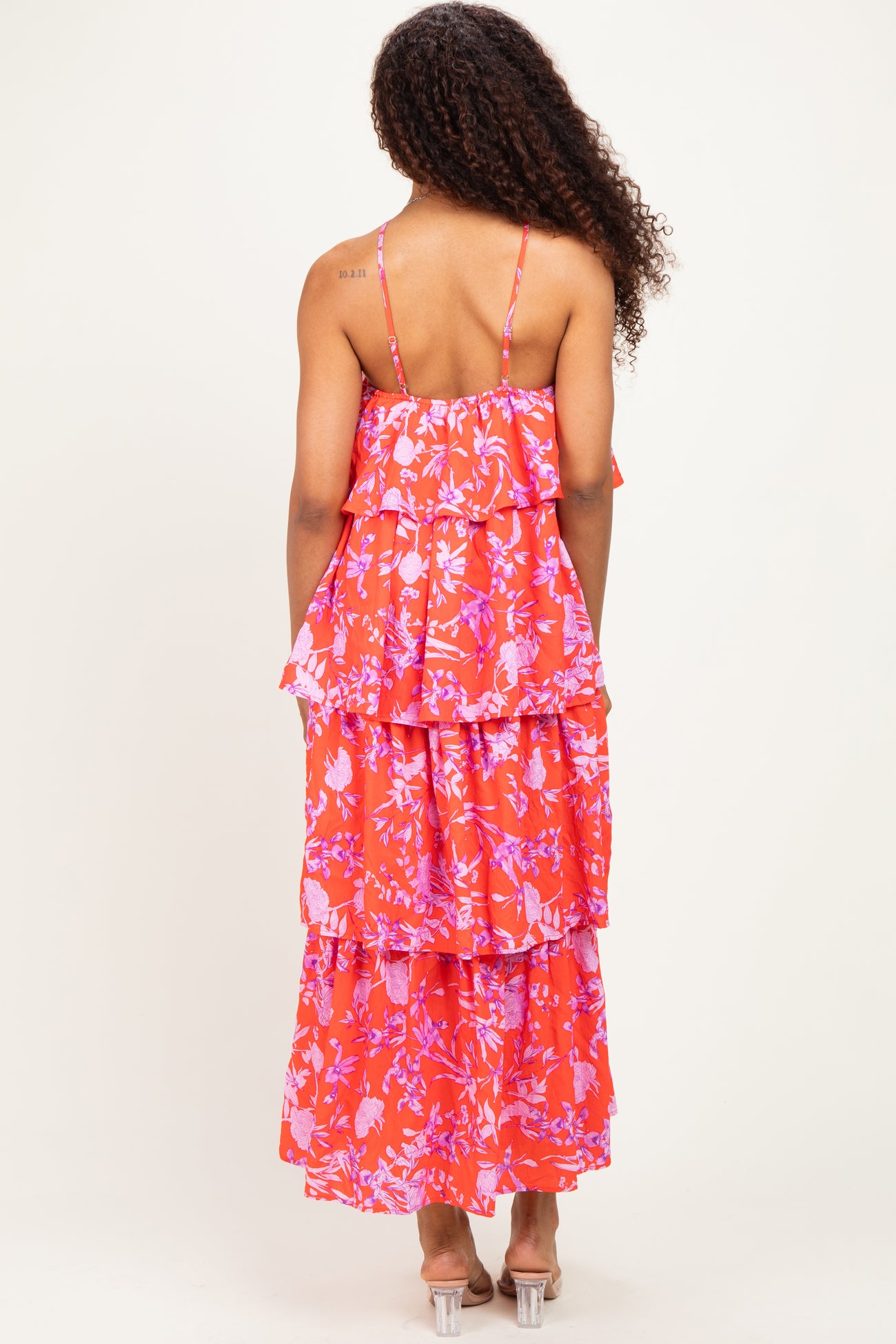 woman wearing a bright pink floral maxi dress with tiered ruffles and thin straps, viewed from the back