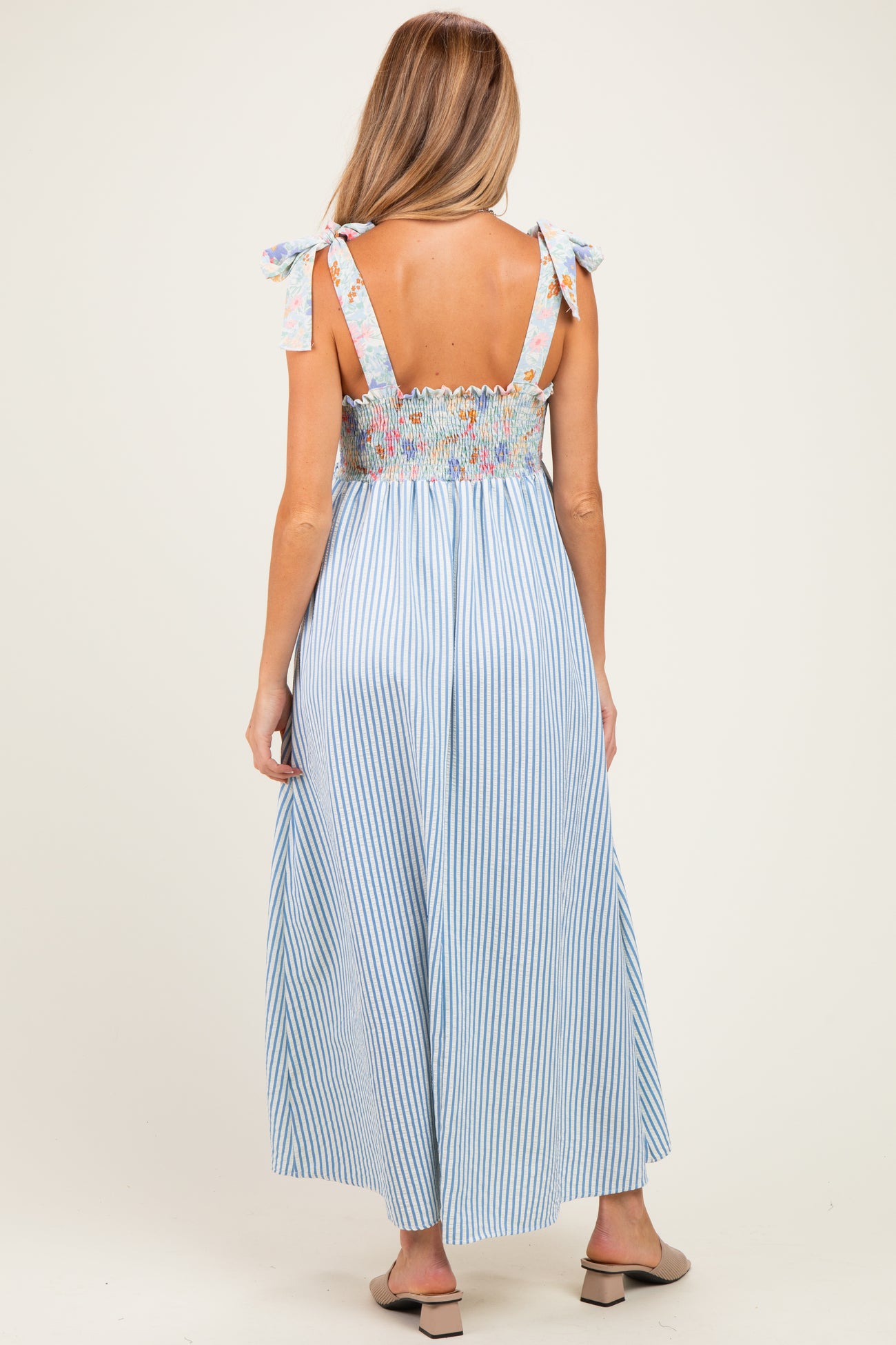 woman wearing a blue and white striped maternity maxi dress with floral smocked bodice and tie straps