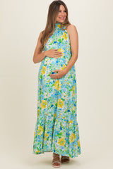 woman wearing a floral maternity maxi dress in shades of blue and yellow, holding her baby bump