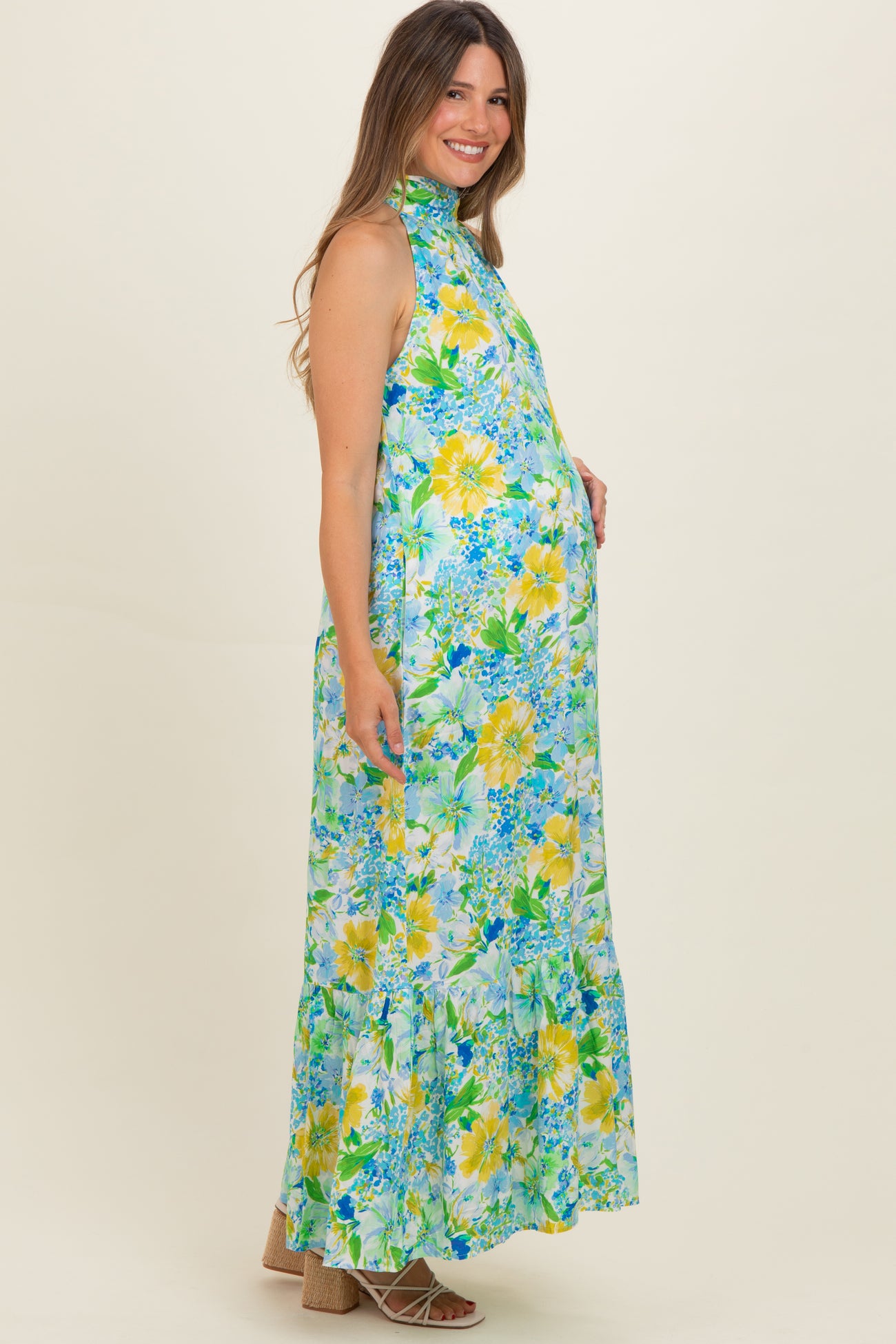 woman wearing a floral sleeveless maternity dress with a high neck and tiered hem, showcasing her baby bump