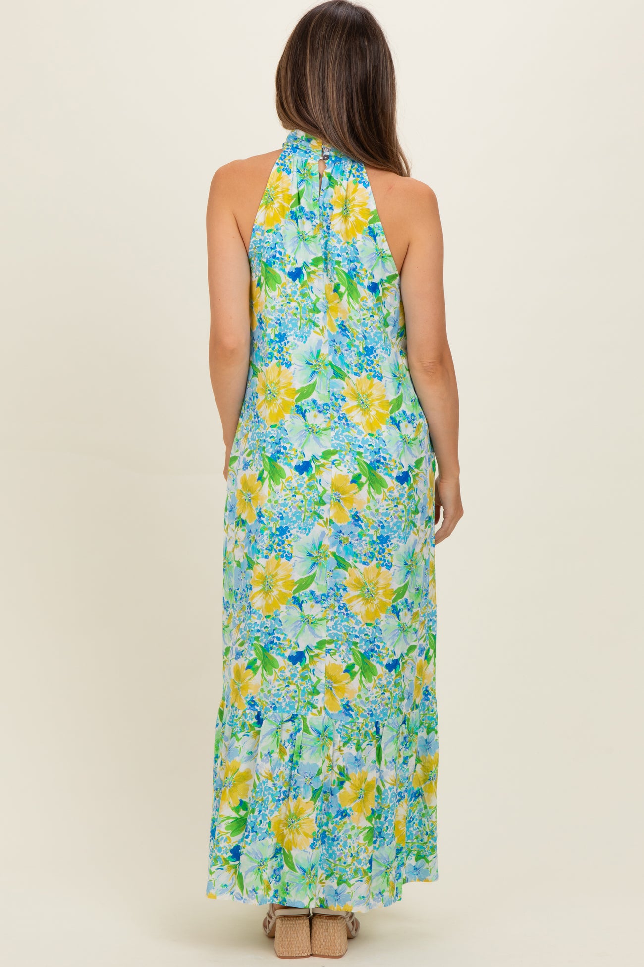 woman wearing a floral halter maternity maxi dress in blue and yellow with a flowing skirt and a fitted bodice