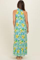 woman wearing a floral halter maternity maxi dress in blue and yellow with a flowing skirt and a fitted bodice
