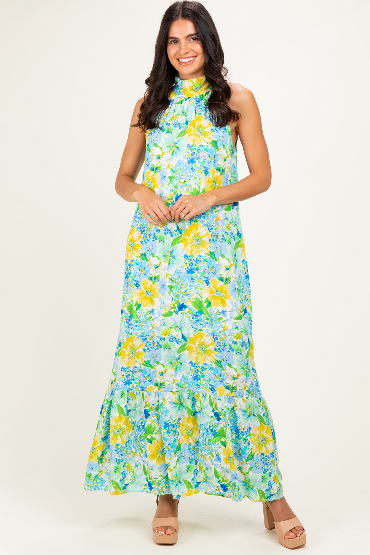 woman wearing a floral maxi dress in greens and yellows with a halter neck and tiered hem