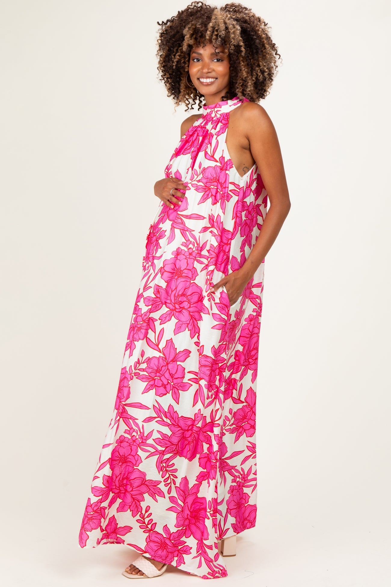 woman wearing a floral pink maternity maxi dress with a halter neck and pockets, showcasing her baby bump