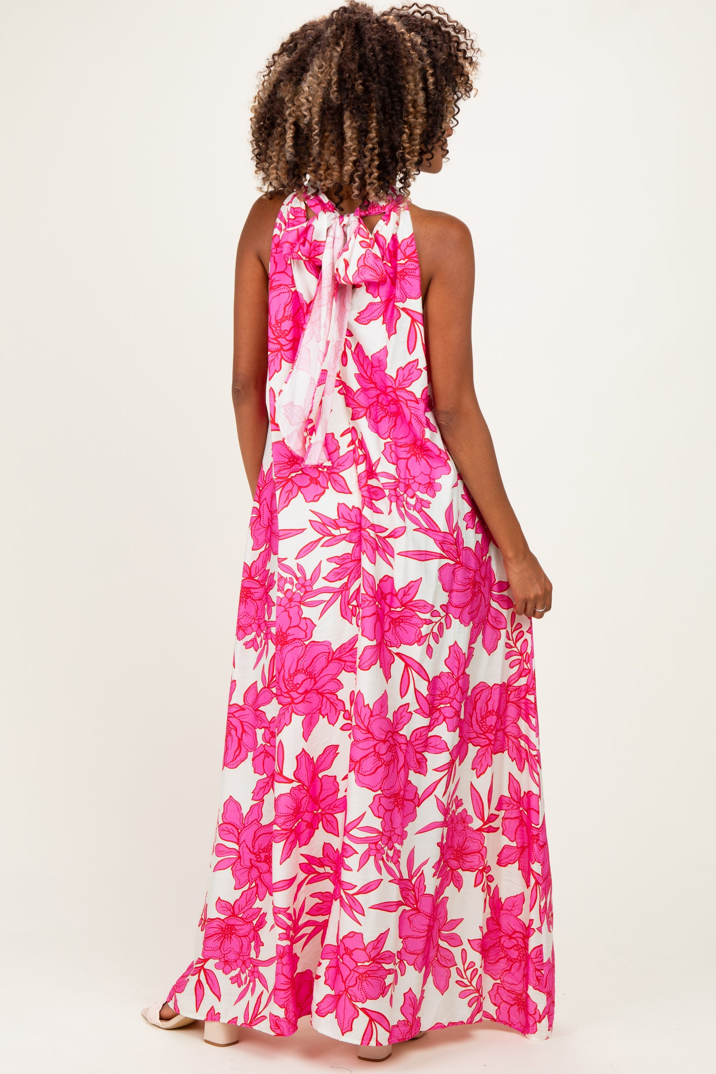 woman wearing a pink floral maxi maternity dress with a halter neckline and open back