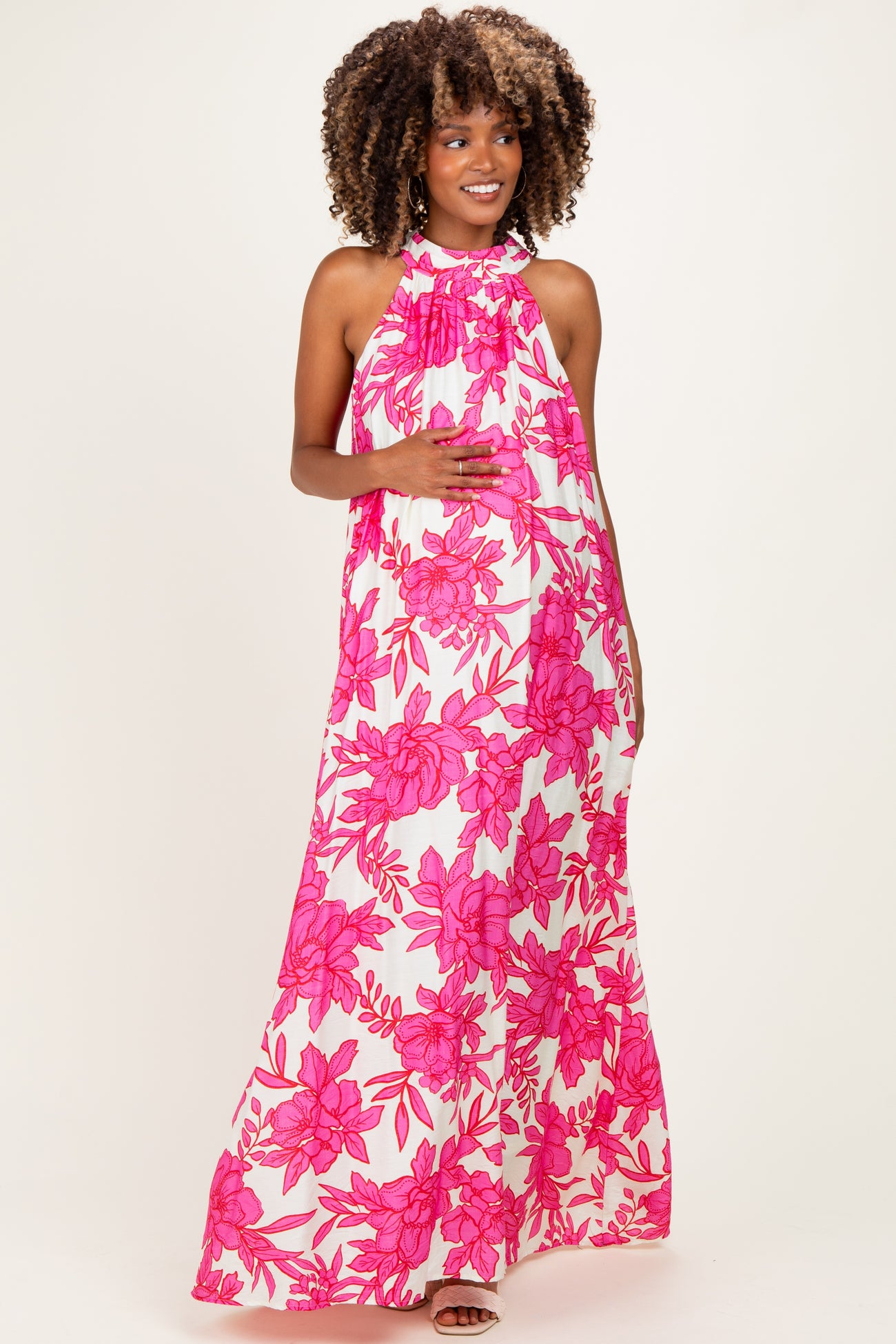 woman wearing a pink floral halter maxi dress and holding her baby bump