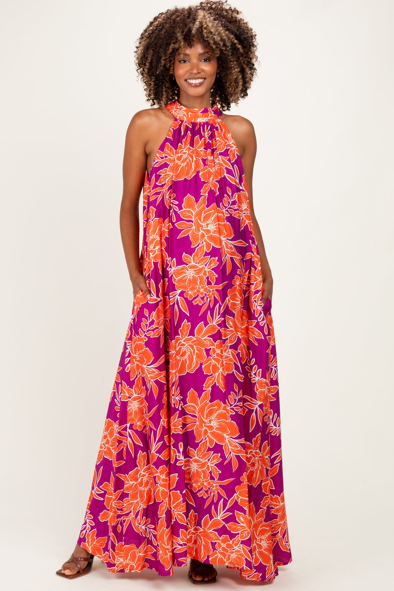 woman wearing a flowy purple maternity dress with bright orange floral pattern and halter neckline, smiling and posing