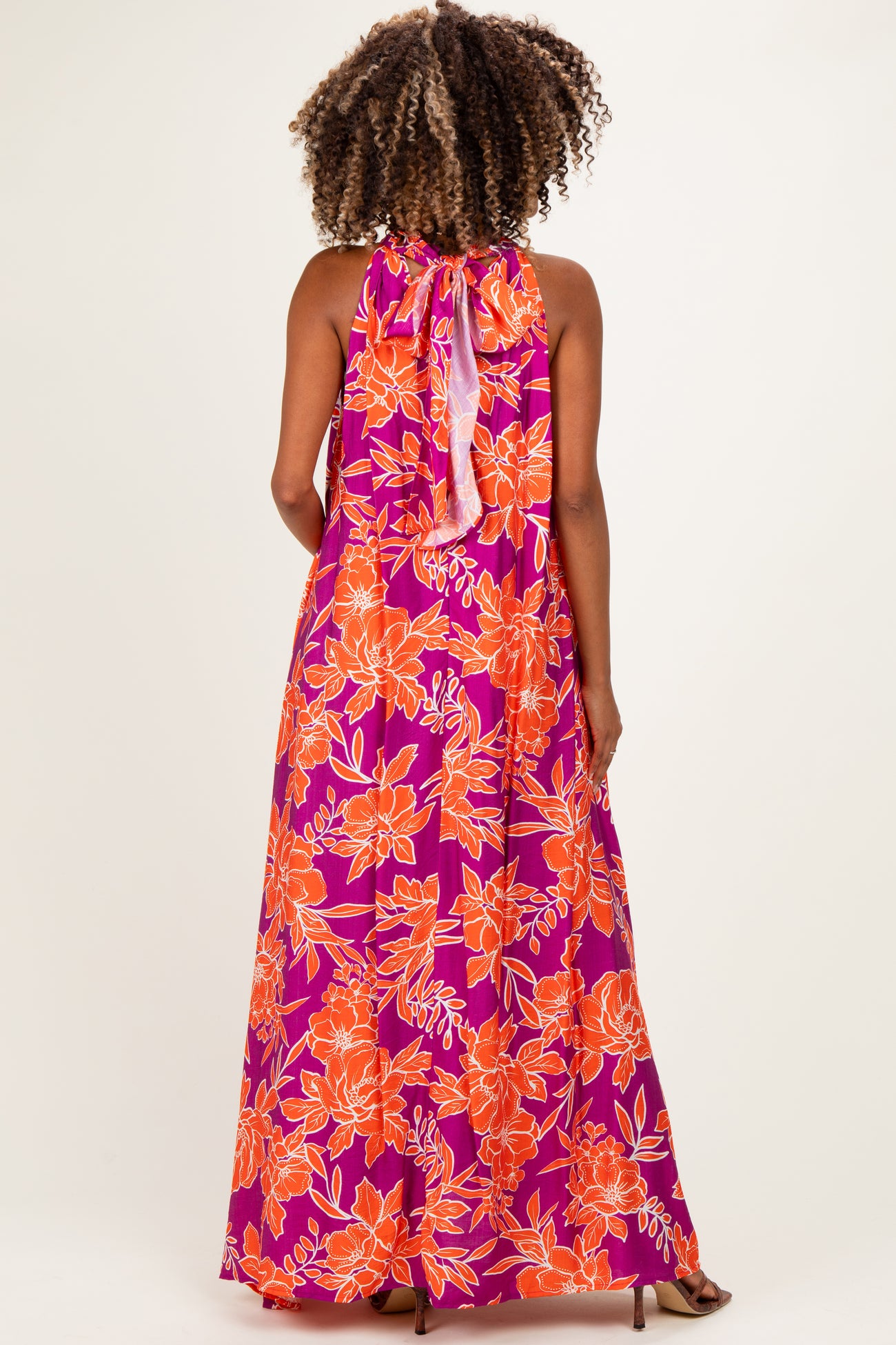 woman wearing a vibrant purple and orange floral maternity maxi dress with a halter neck and an open back