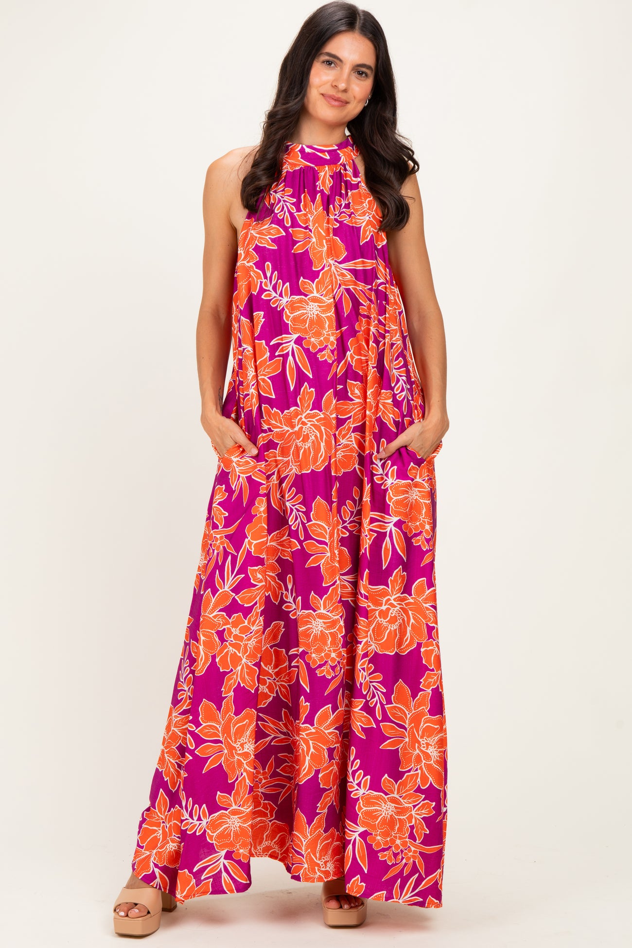 woman wearing a bright pink maxi dress with orange floral print and pockets