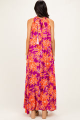 woman wearing a back view of a sleeveless purple maxi dress with orange floral print and a tie closure at the neck
