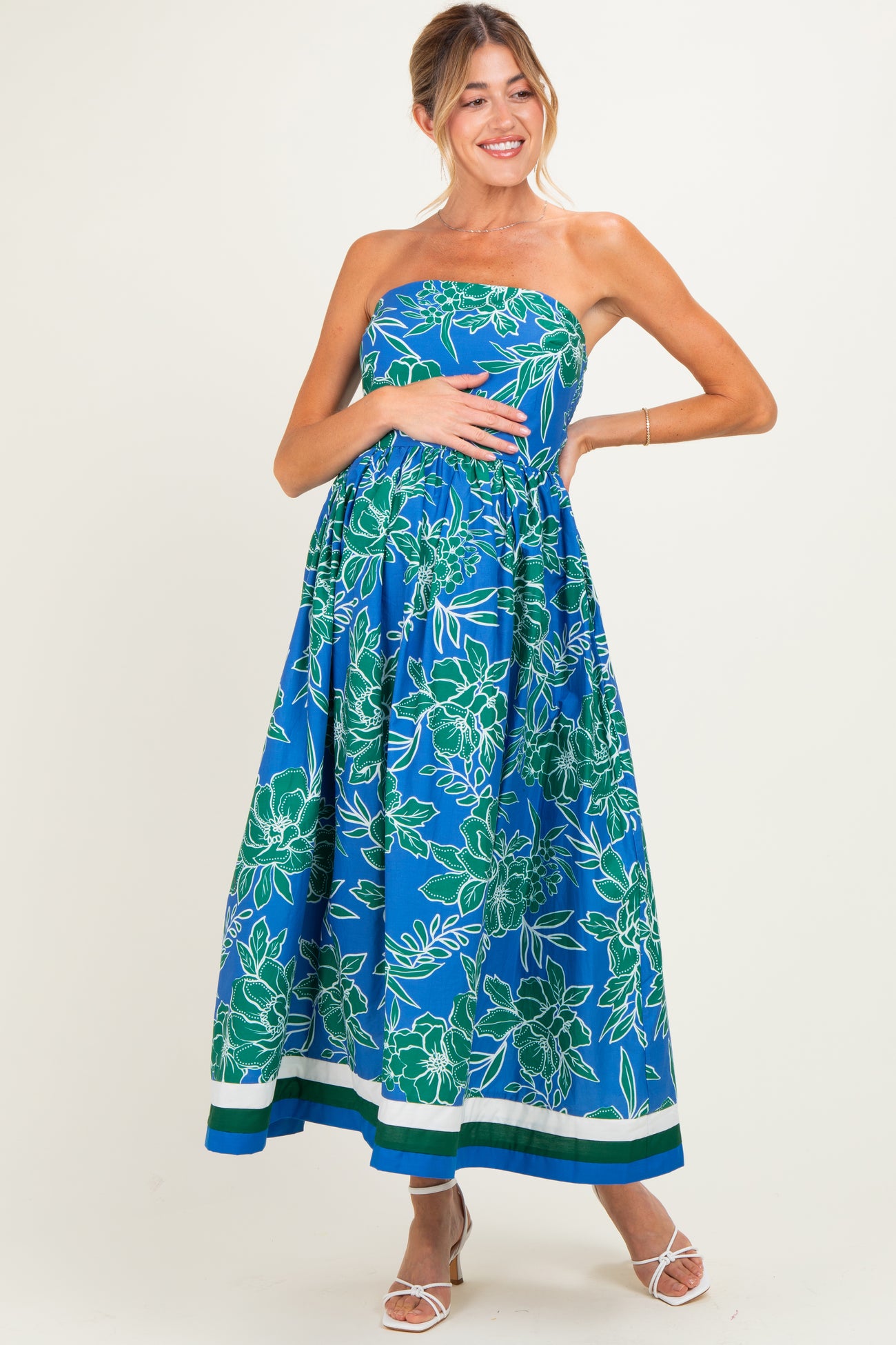 woman wearing a strapless blue floral maternity maxi dress and cradling her baby bump