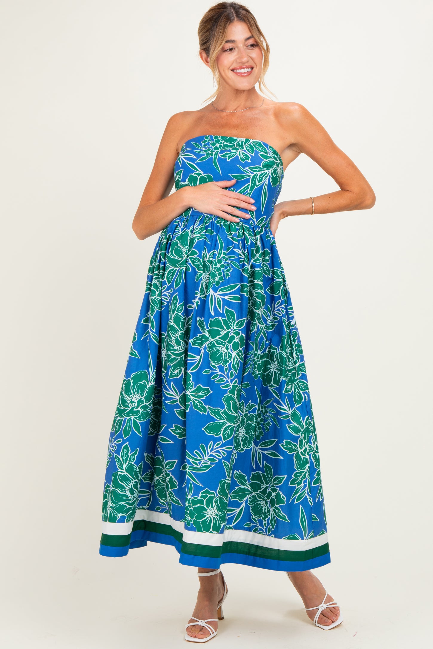 woman wearing a strapless blue floral maternity maxi dress and cradling her baby bump