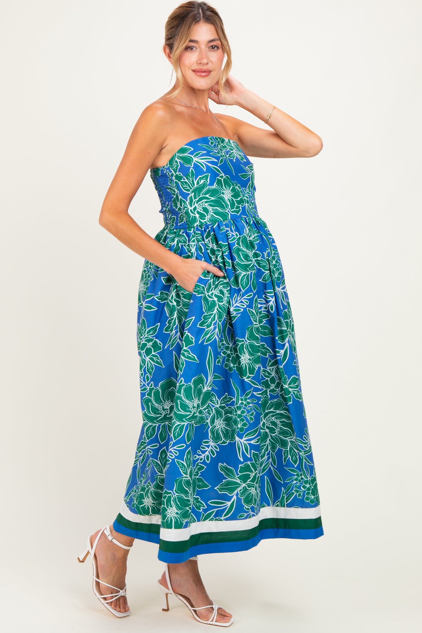 woman wearing a colorful strapless floral print maternity dress with pockets and a gathered waist, showcasing her baby bump