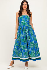 woman wearing a blue floral maxi dress with a fitted bodice and gathered skirt, styled with white heels