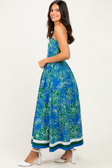woman wearing a strapless blue maxi dress with green floral print and white heels
