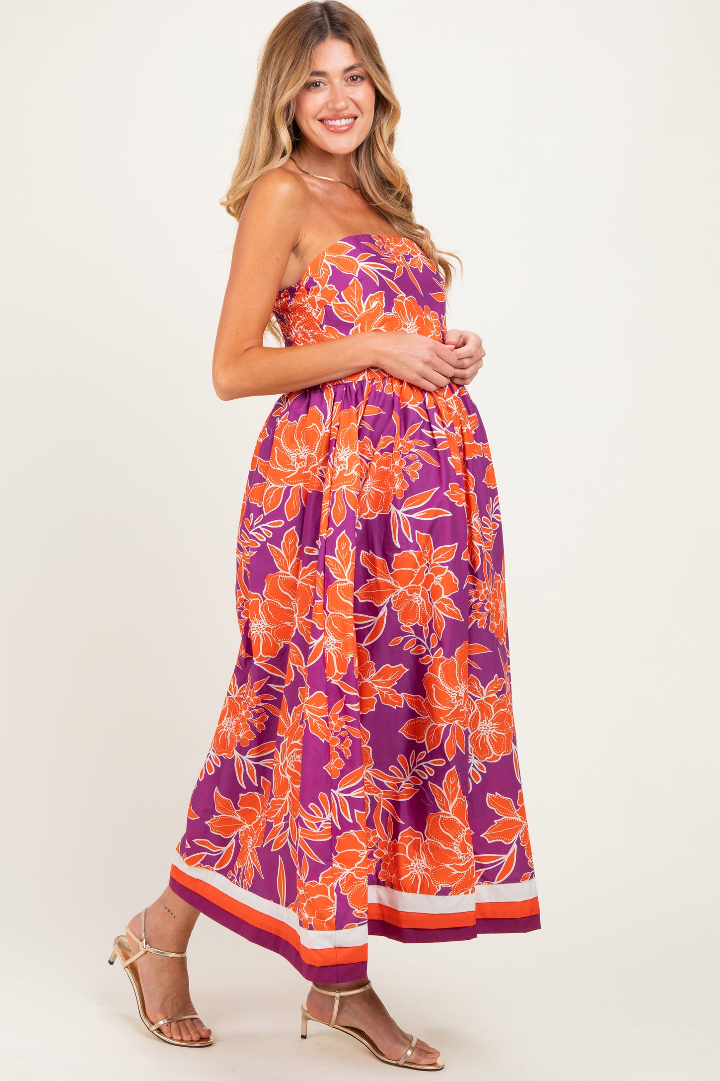 woman wearing a vibrant purple strapless maxi dress with orange floral prints, showing off her baby bump