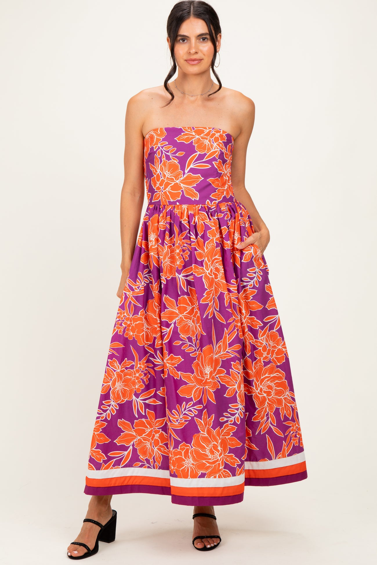 woman wearing a strapless purple maxi dress with orange floral print and pockets, standing in a relaxed pose