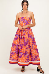 woman wearing a strapless purple maxi dress with orange floral print and a cinched waist, standing in black strappy heels
