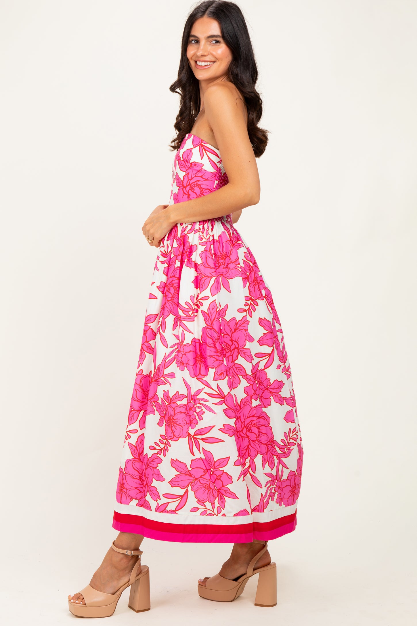 woman wearing a strapless maxi dress with bold pink floral print and a pink trim at the hem