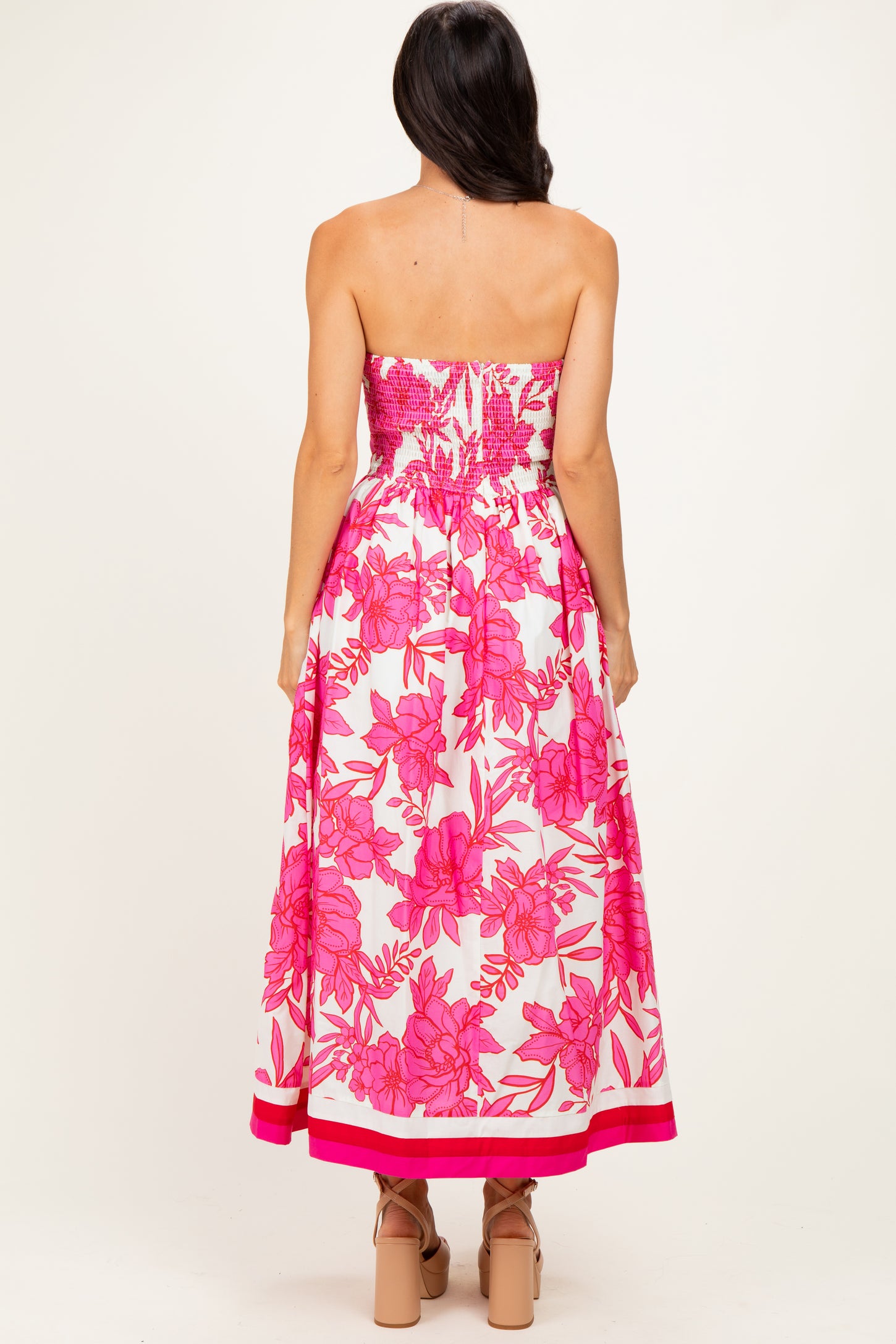 woman wearing a strapless pink floral maxi dress with a smocked bodice and a flared skirt, seen from the back