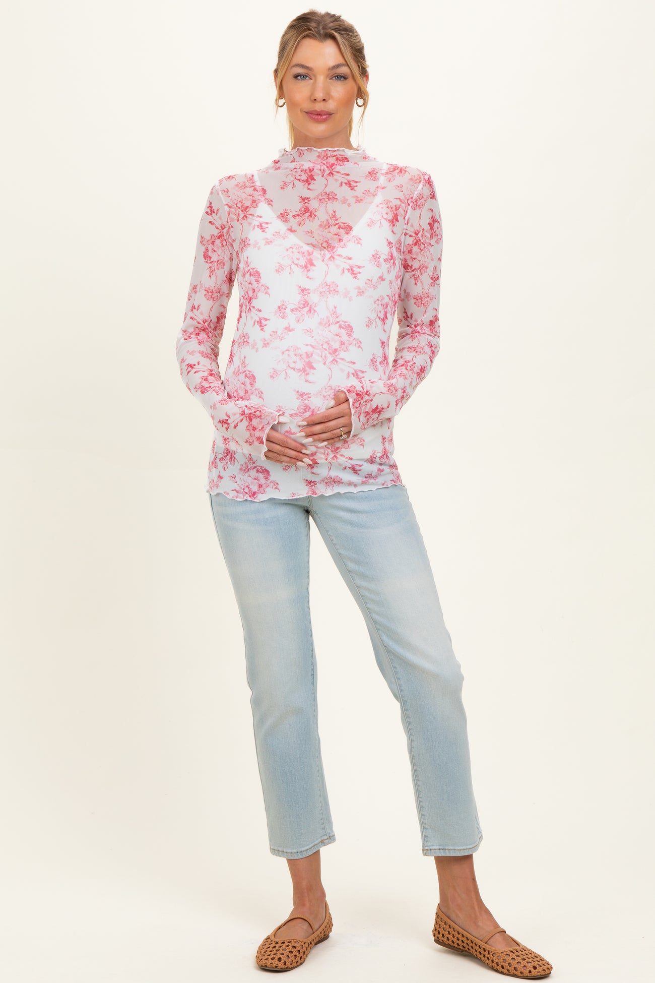 woman wearing a sheer floral maternity top in pink and white with a baby bump, paired with light blue jeans