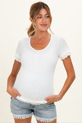woman wearing a white short sleeve maternity top with button detail and ribbed texture, cradling her baby bump